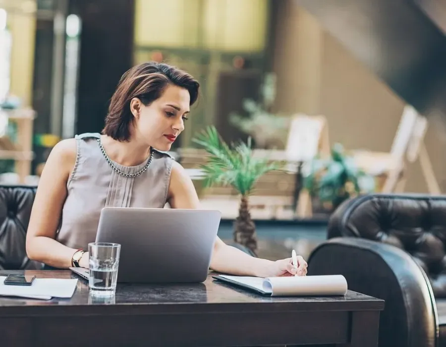 Paralegal seated in lobby in front of laptop while taking notes on notepad